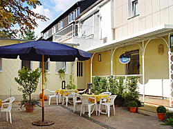 Weiße Stühle und Tische unter Sonnenschirmen im Hof hinter dem Haus