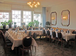 Eingedeckte Tische im Restaurant unter einem Kronleuchter vor hohen Fenstern