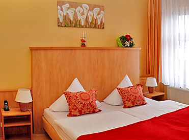 Hotelzimmer mit Doppelbett, hölzernem Kopfteil, orangefarbenen Kissen und Nachttischlampen