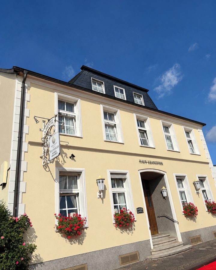 Das Hotel Kranefoer mit gelber Fassade, weißen Sprossenfenstern, roten Geranien in den Blumenkästen und dem Hotelschild neben dem Eingang